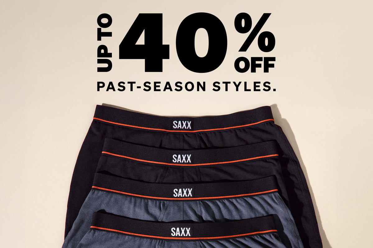 Four pairs of SAXX men's boxer briefs in black and gray are stacked diagonally on a beige background, with a large promotional text overlay at the top reading 'UP TO 40% OFF PAST-SEASON STYLES.'.
