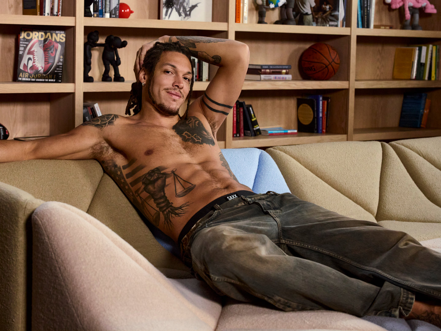 SAXX Gamechanger and Professional Basketball player Aaron Gordon lying on a couch in a room with bookshelves and sports balls.
