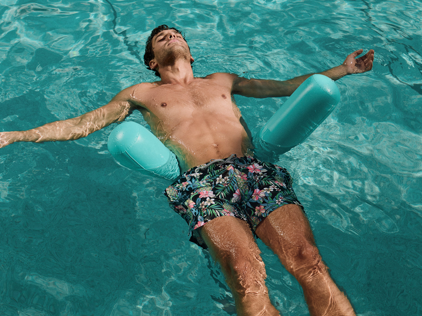 Man floating in a pool with floral swim shorts and a blue inflatable ring.