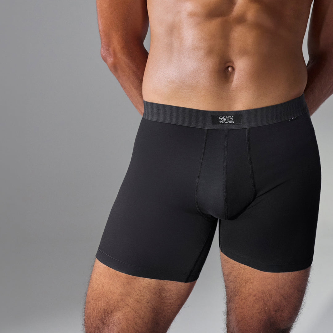 A close-up of a male model's lower torso wearing black boxer briefs with a dark gray elastic waistband. The brand name 'BROOKS' is visible on the front center of the waistband.