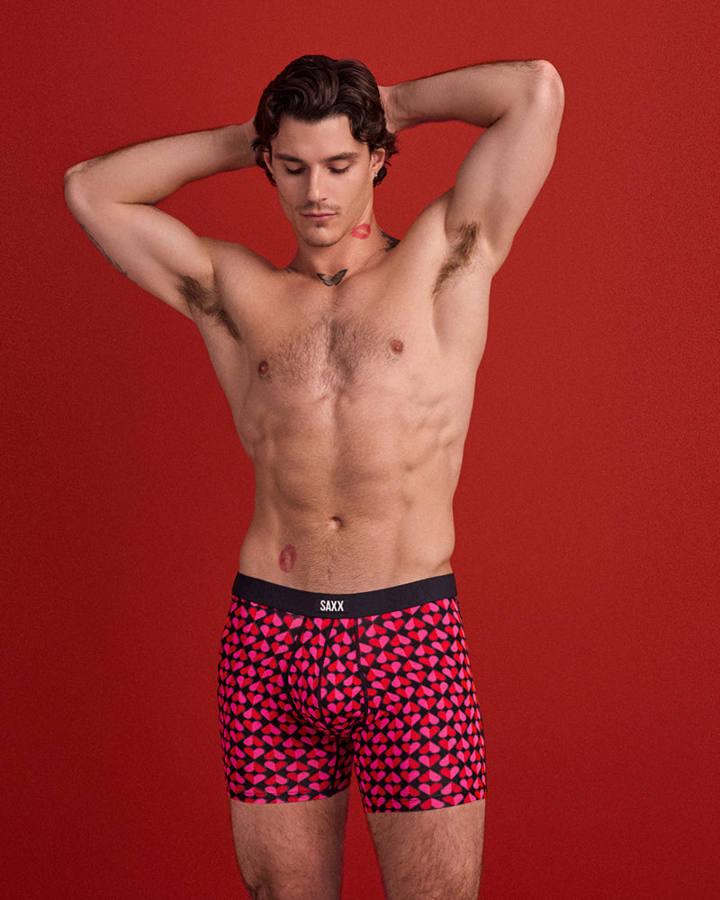 Man wearing red and black patterned boxer briefs with a red background