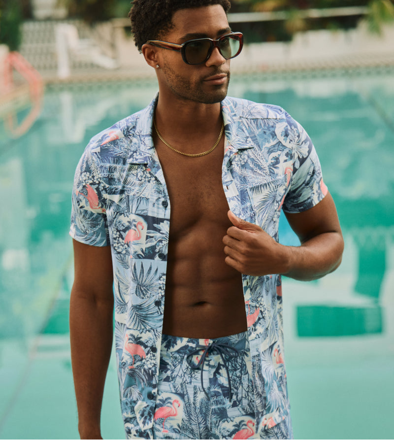 Man in unbuttoned floral shirt and matching shorts standing in front of pool
