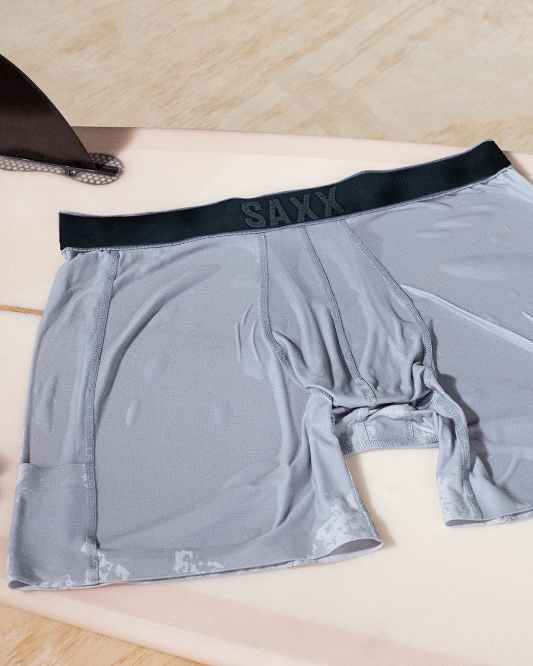 Grey boxer briefs laid flat on a surfboard showing quick drying fabric and water ready performance