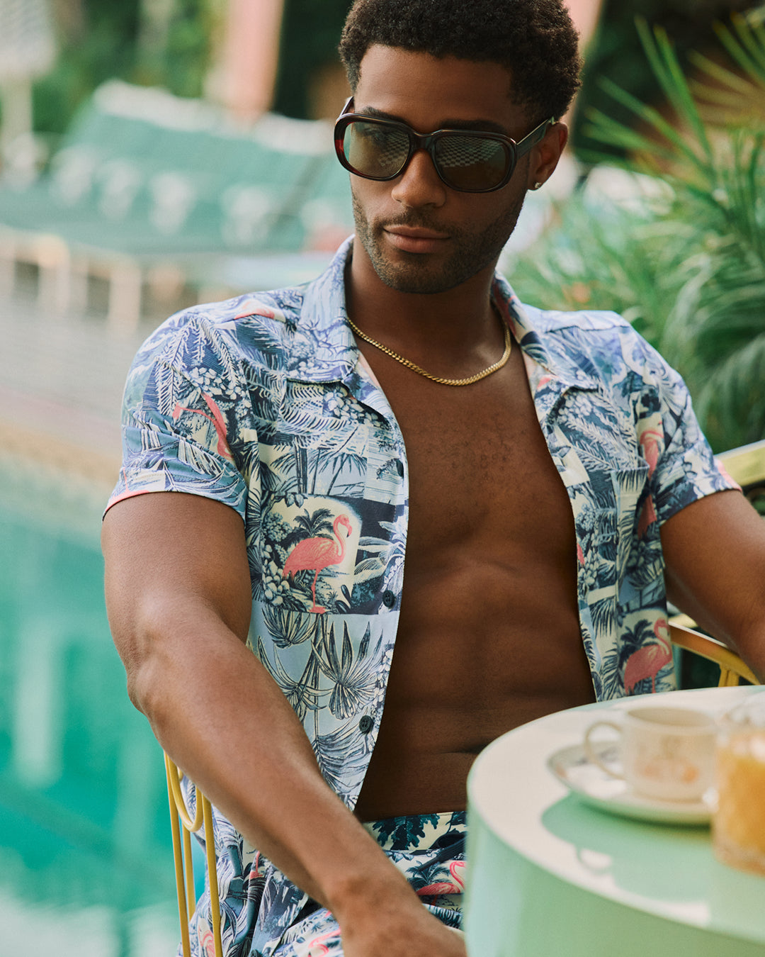 Man wearing a tropical patterned shirt sitting outdoors with plants in the background