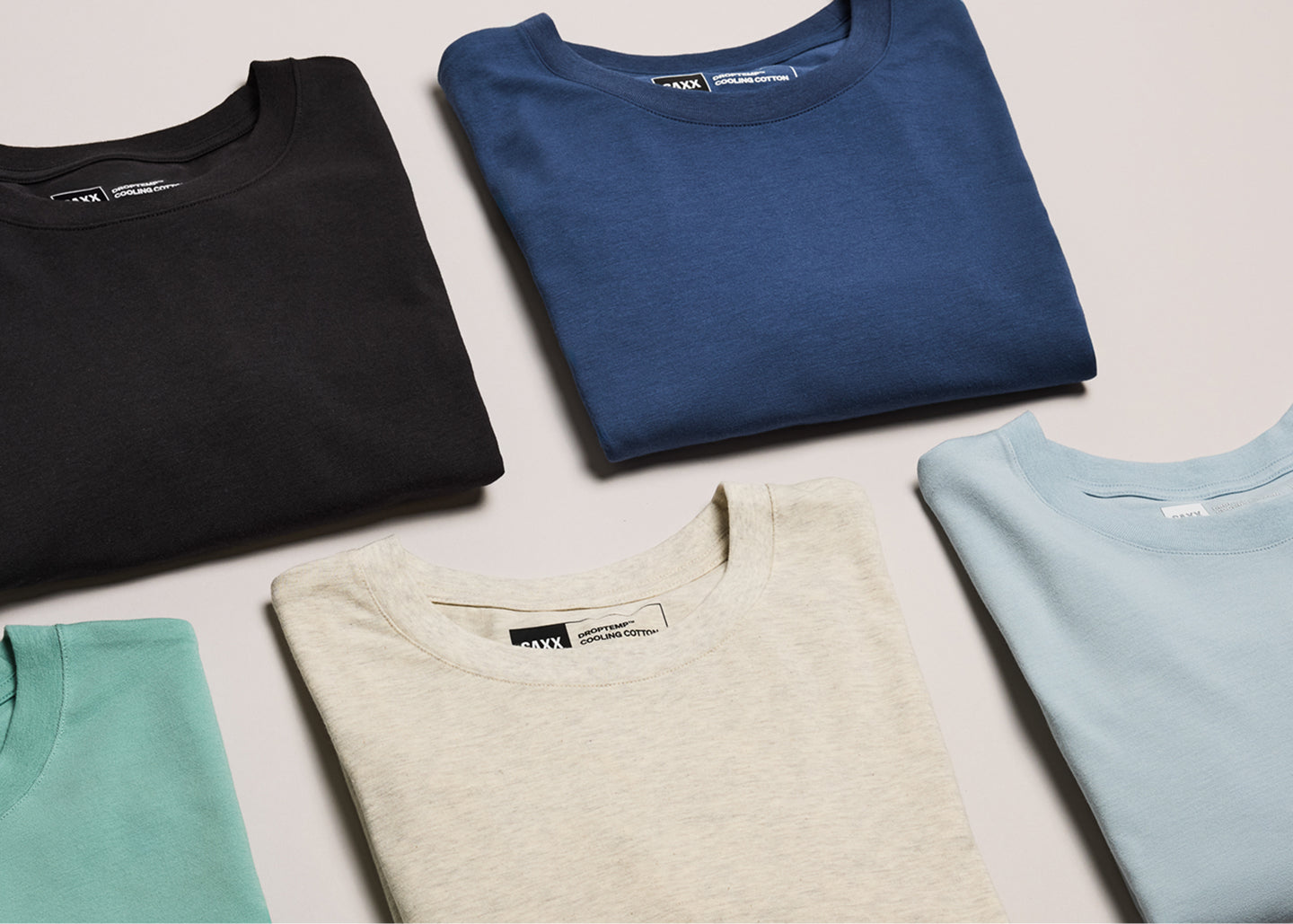 Folded t-shirts in black, blue, beige, and light blue on a neutral background