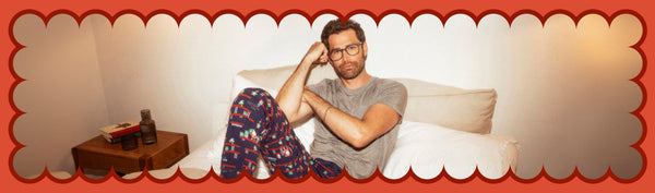 Man wearing gray Sleep tee and pajama pants in a holiday print while laying in bed