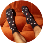 Man wearing black socks in a reindeer print with his feet on a red velvet couch