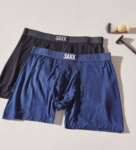 Two boxer briefs in black and blue next to a razor and shaving brush