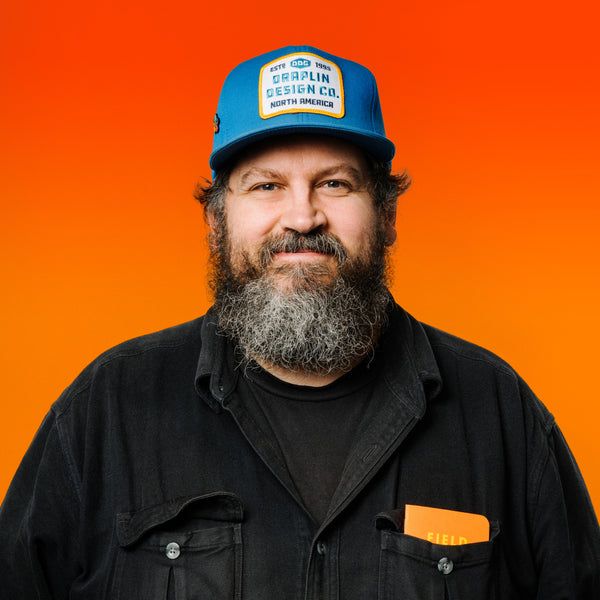 Photo of artist Aaron James Draplin in front of an orange background