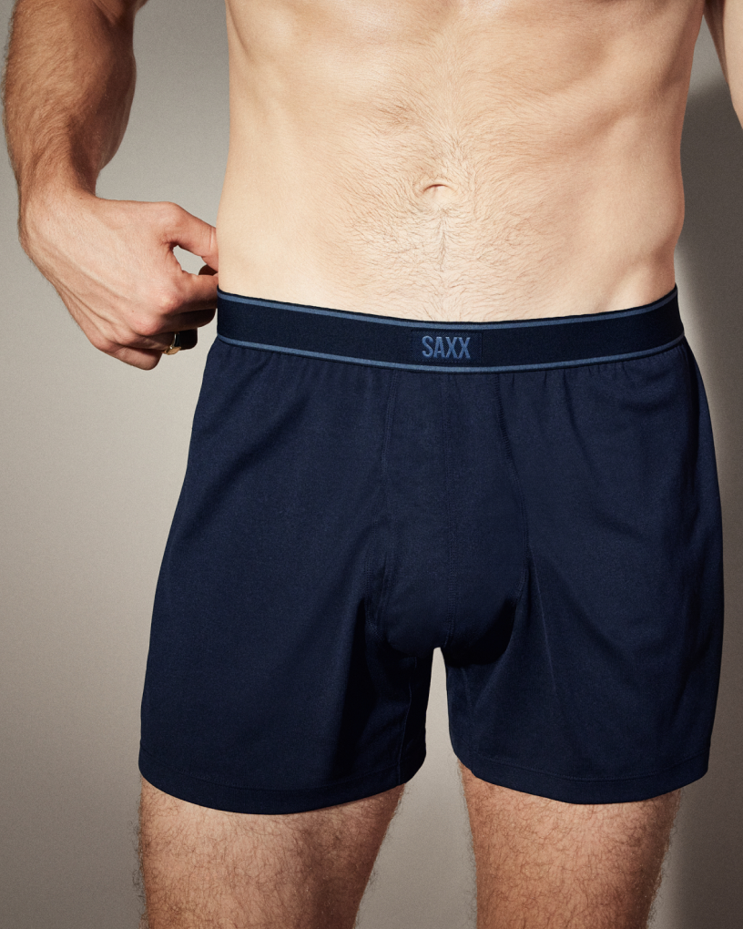 Closeup on man’s torso in navy SAXX Loose Fit Boxers, one hand on waistband.