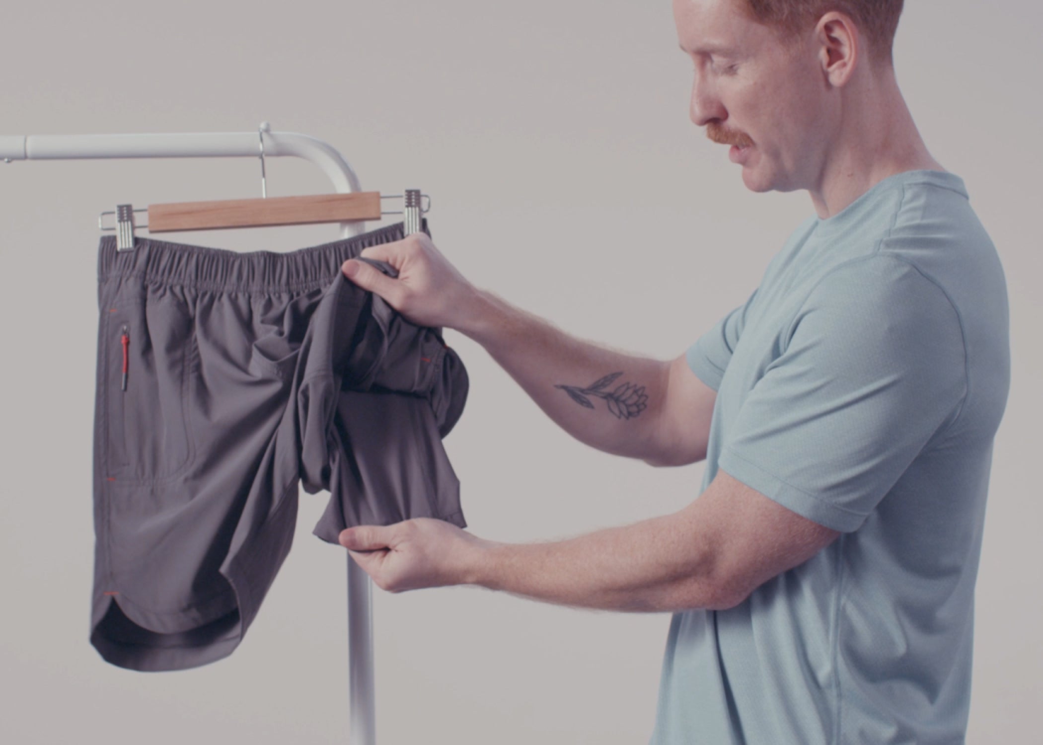 A man in a grey SAXX tee showing the liner in a pair of grey SAXX Gainmaker Shorts hanging on a rack. 