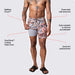 Man in grey red floral print swim shorts and sandals lifting short leg to reveal liner