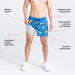 Man in beer game print swim shorts and shoes lifting short leg to reveal liner