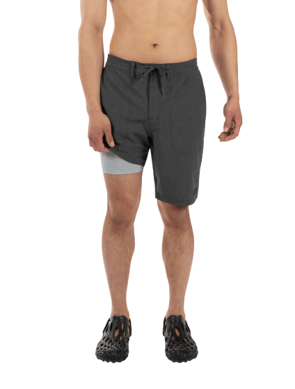 Shirtless man in grey shorts and sandals lifting short leg to reveal liner